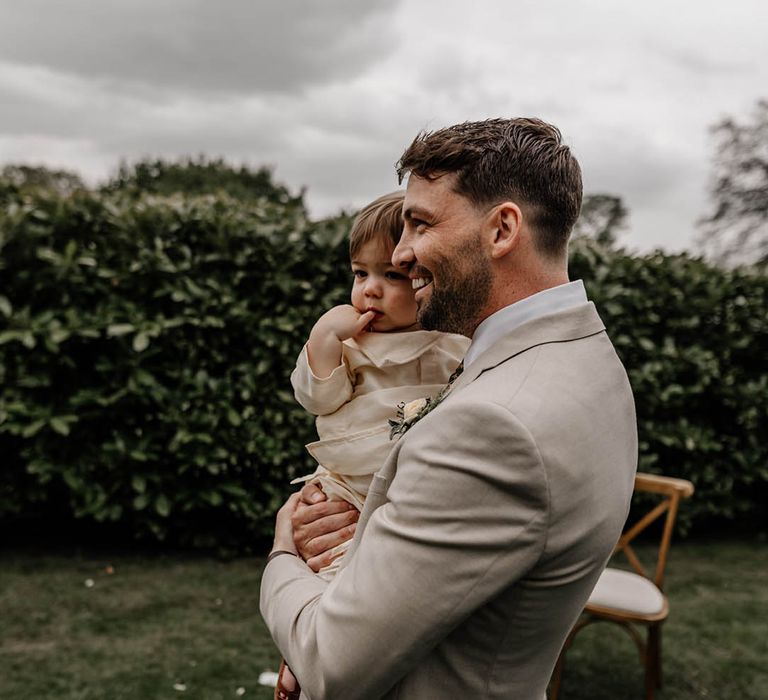 Groom in a beige suit holding his son at the altar 