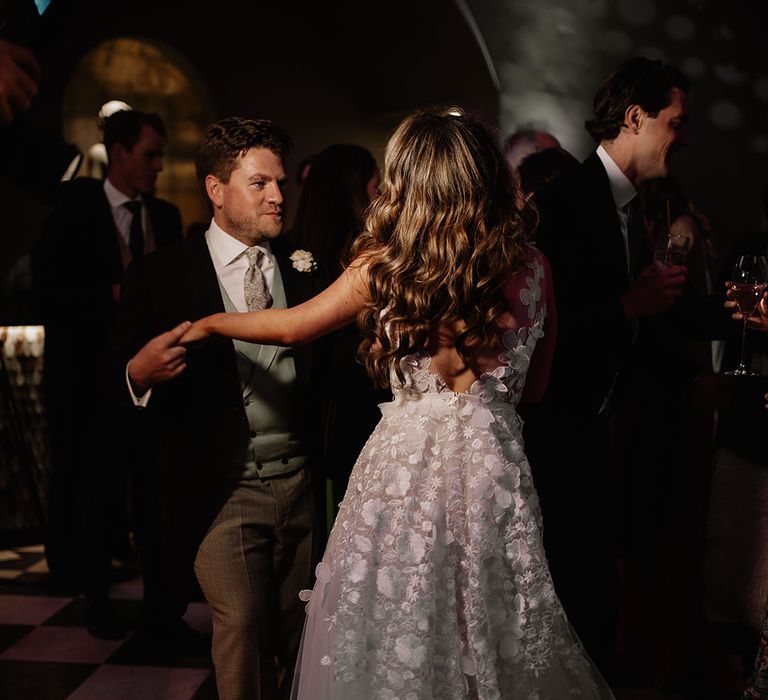 Bride and groom dance together on the dance floor with bride in flower applique wedding dress and groom in morning suit 