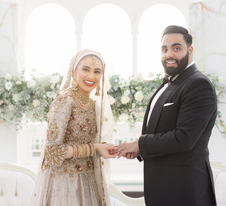 Bride wears traditional saree in gold and silver as she holds her grooms hands who wears black tie 