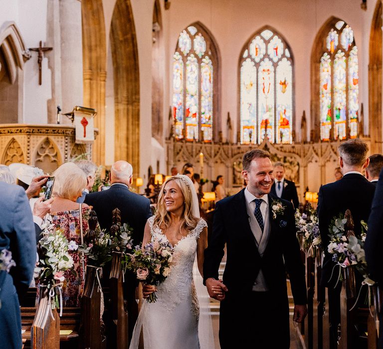 Bride and groom smile at their wedding guests as they walk back down the aisle as a married couple 