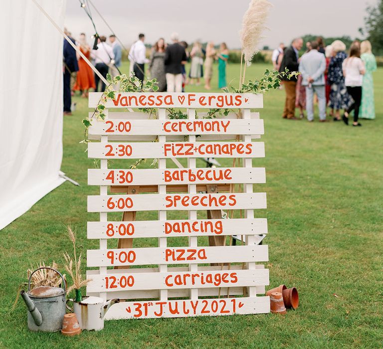 DIY Order Of The Day pallet painted white with orange writing and floral decor 