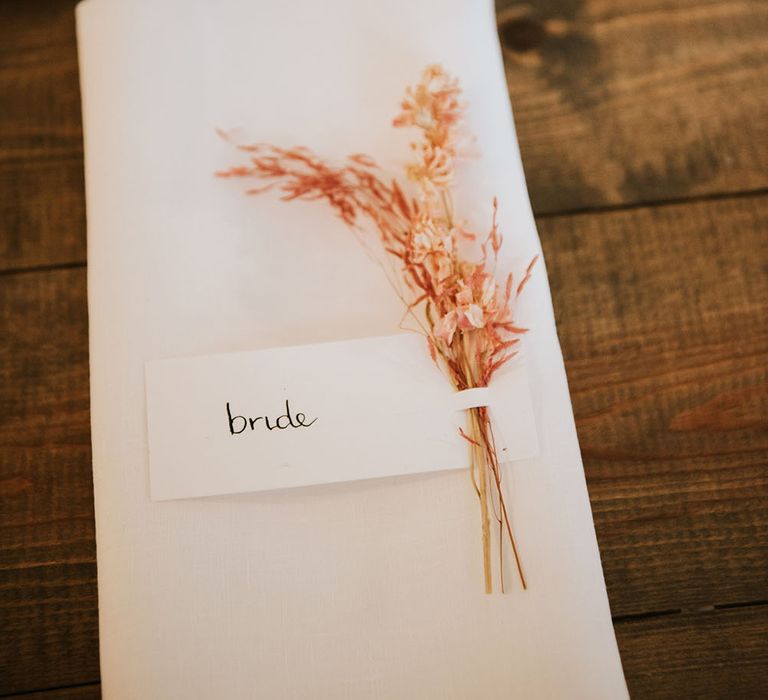 White napkin with 'Bride' name card complete with dried floral decor in light pink 