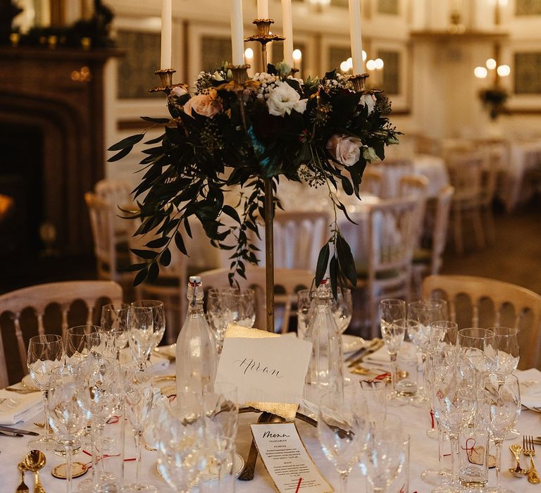 Wedding reception tablescape complete with white tablecloths and floral bouquets set up on gold candle pillars 