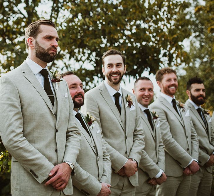 Groom becomes emotional seeing his bride for the first time on wedding day as he stands besides his grooms who wear matching stone beige three piece suits 