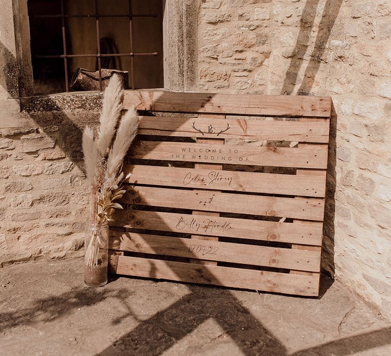 Wooden pallet Welcome Sign finished with engraved writing beside dried pampas grass in white vase