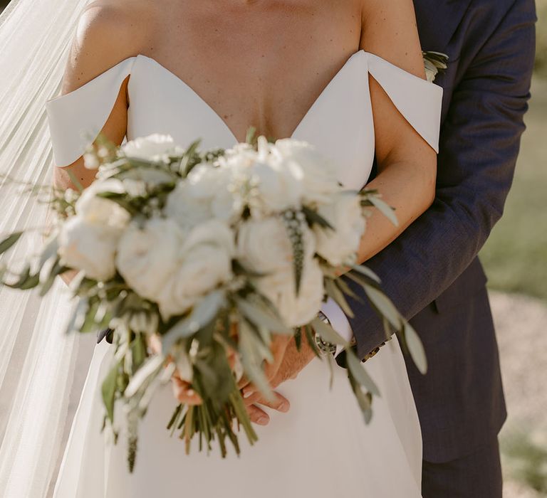 Bride wears floor-length veil in her blonde hair and carries white rose floral bouquet 