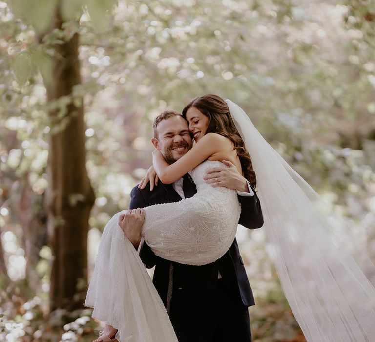 Groom carries his bride through the woods for back garden wedding