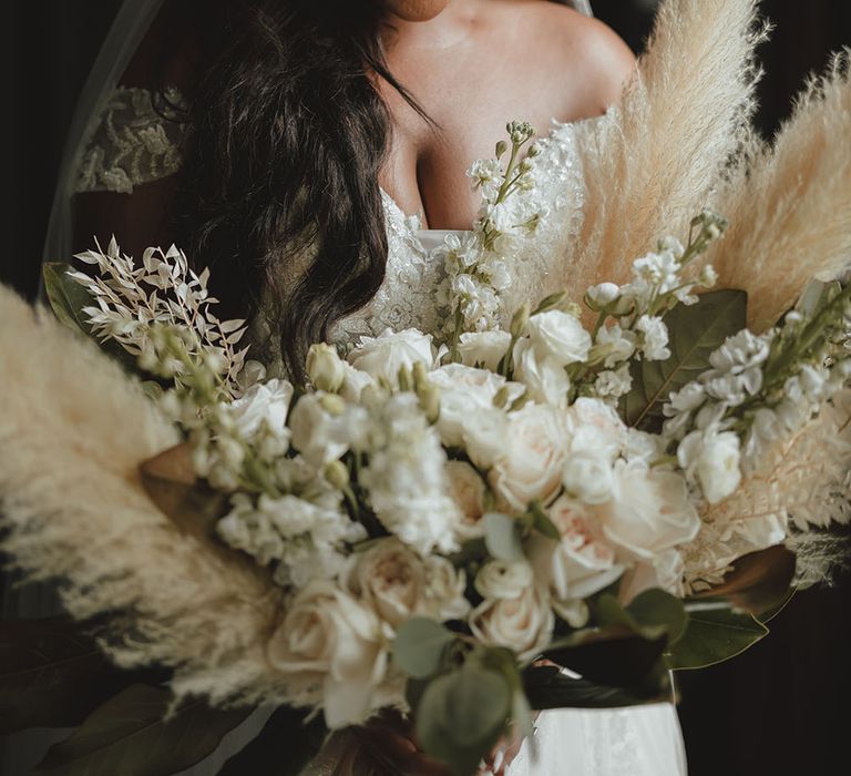 Black bride holds extravagant pampas grass floral bouquet filled with white flowers and green foliage 