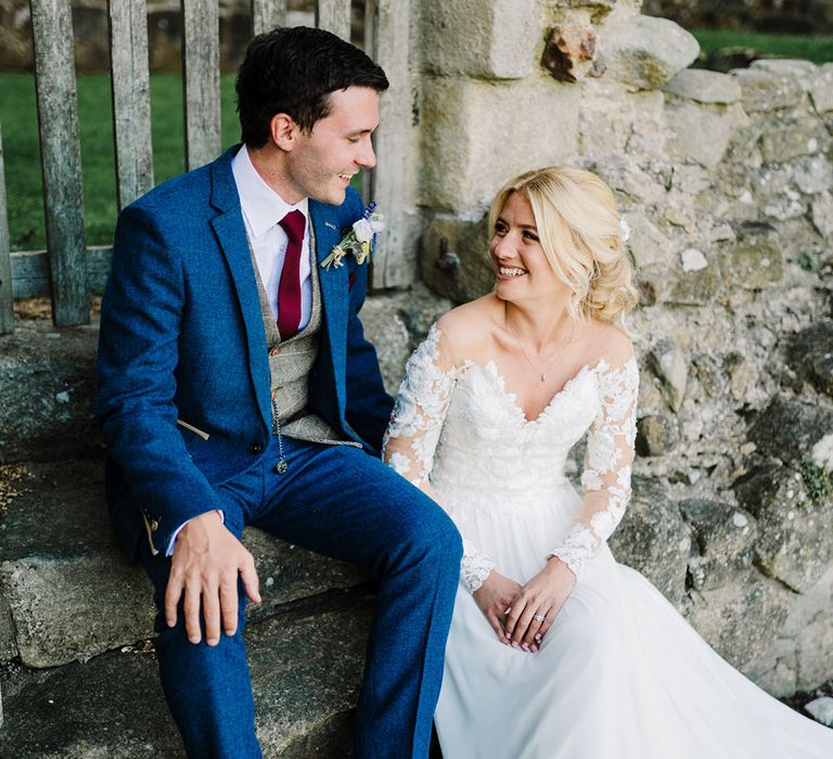 Bride wears long sleeve lace Pronovias wedding dress and sits beside her groom in three piece suit 