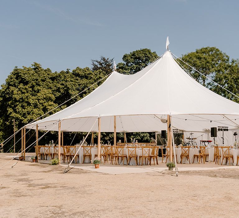 Outdoor wedding tent for summer wedding with pastel florals and wooden chairs 