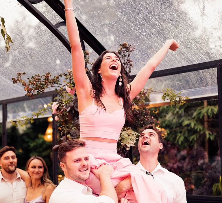 Two wedding guests lift up another guest on their shoulders