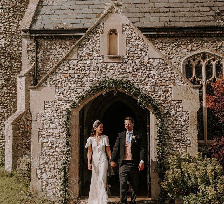 Bride in a button Ghost wedding dress with the groom in a morning suit with a pink waistcoat for their church wedding ceremony 