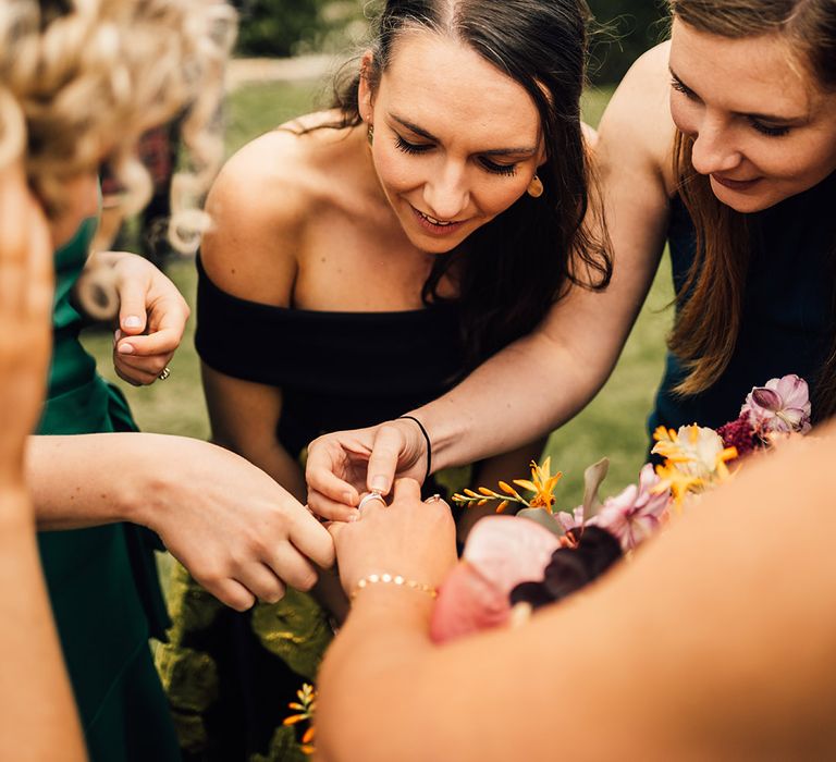 Bridesmaids gather around bride as they look at her wedding band after ceremony 