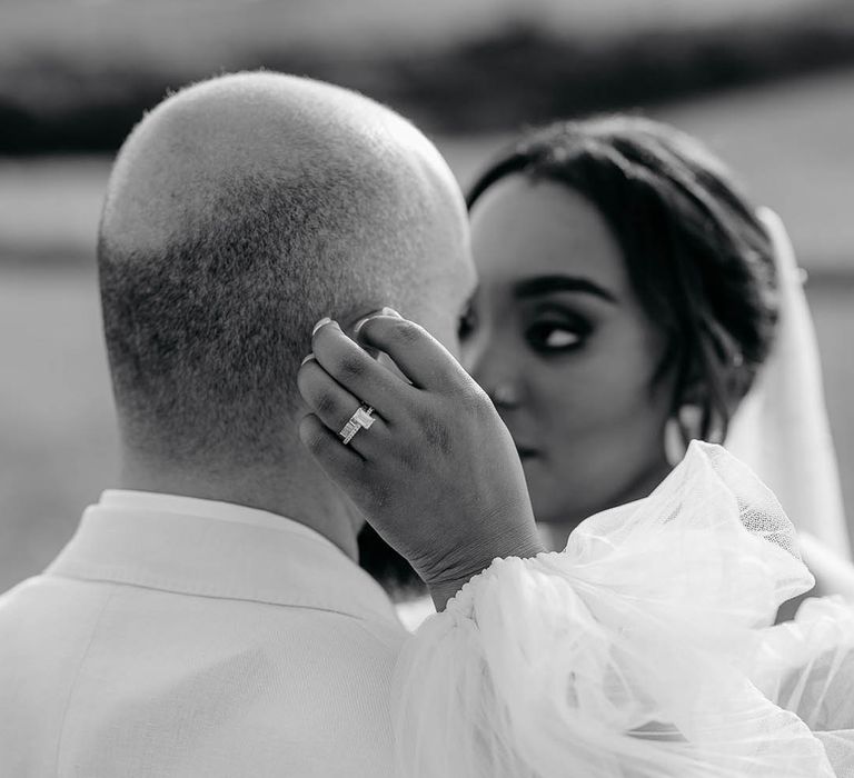 Bride shows off wedding ring  and engagement ring whilst holding Groom’s head in sheer-sleeved dress