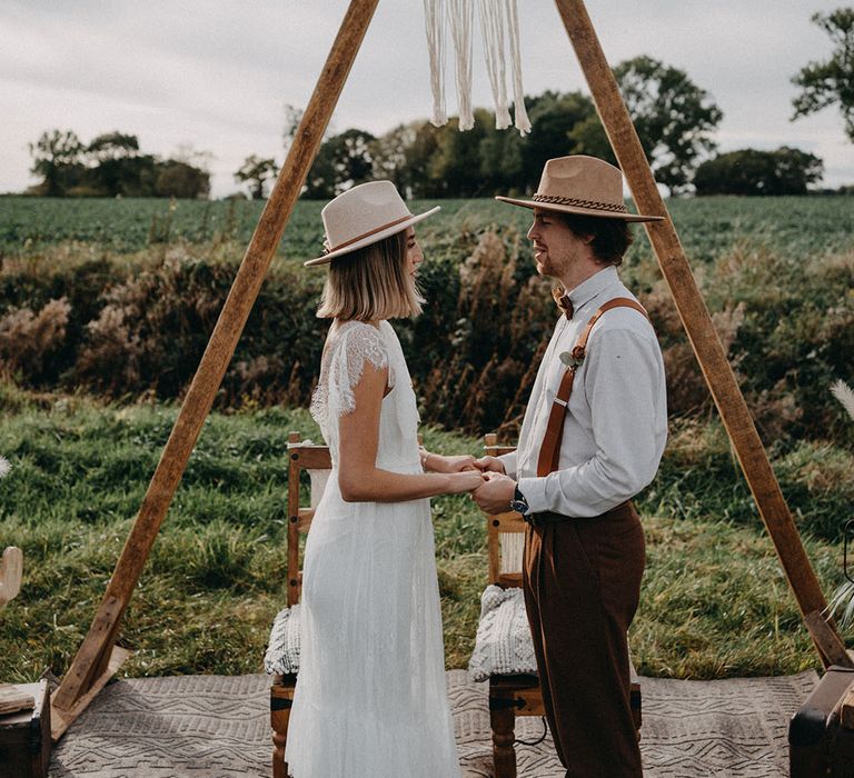 The bride and groom stand holding hands at the altar space for their outdoor wedding 