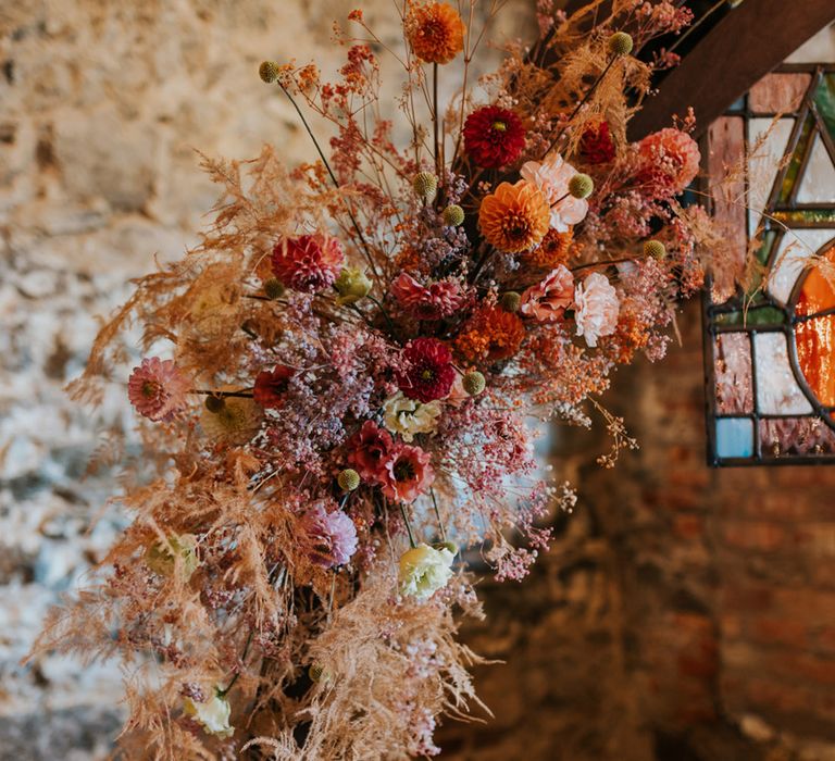 Red, orange, and pink wedding flowers with dried grass decorating the altar 