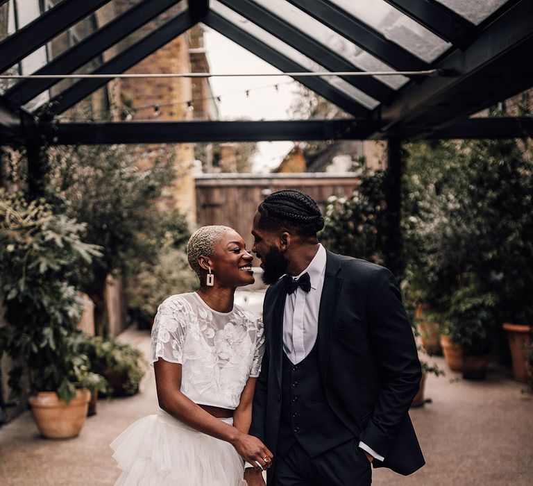 Bride and Groom holding hands in a black wedding suit and a bridal two piece set featuring embroidered floral details and ruffles