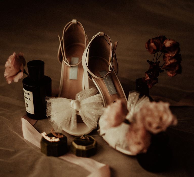 Open toe wedding heels with large polka dot sheer bow on the front, dried roses, a dark perfume bottle and gold wedding jewellery 