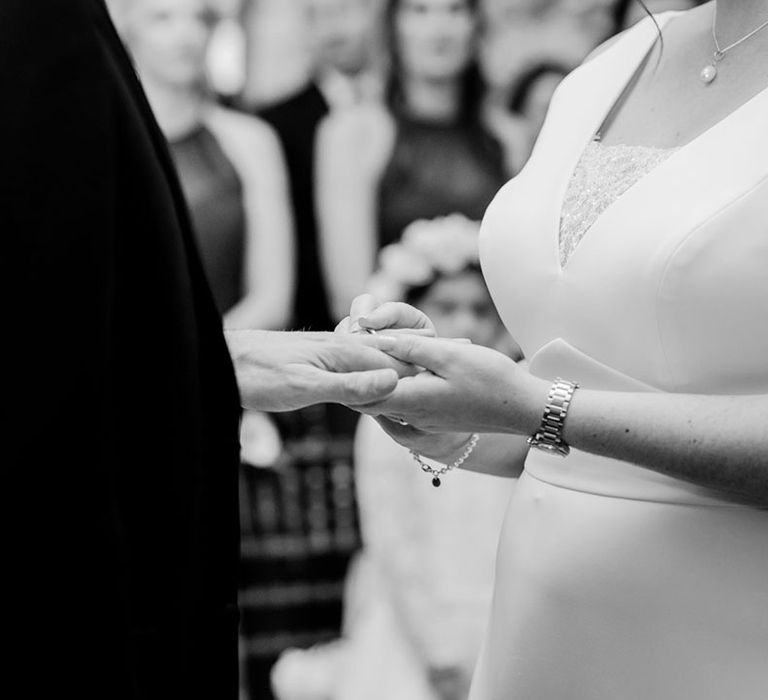 Bride in a classic wedding dress with lace insert putting on the groom's wedding ring for his civil ceremony 