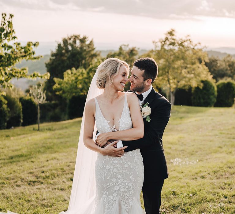 Bride in lace plunge wedding dress beside her groom in black-tie during outdoor couples portraits