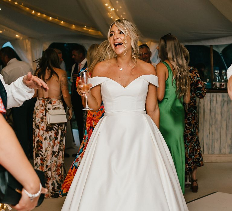 Bride in off-the-shoulder princess wedding dress laughs during marquee wedding reception 