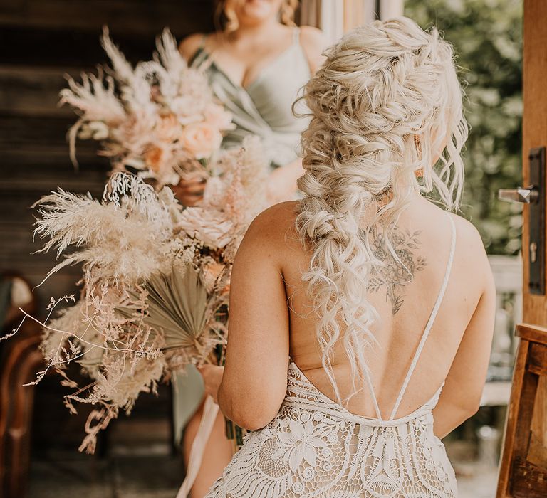 Bride in open back boho lace wedding dress with her platinum blonde hair in an intricate fishtail braid holding an oversized pampas grass wedding bouquet 