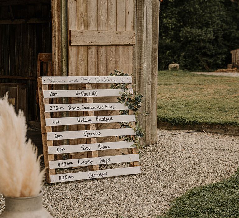 DIY wooden pallet wedding order of the day sign with foliage decorating it at the entrance of the venue 