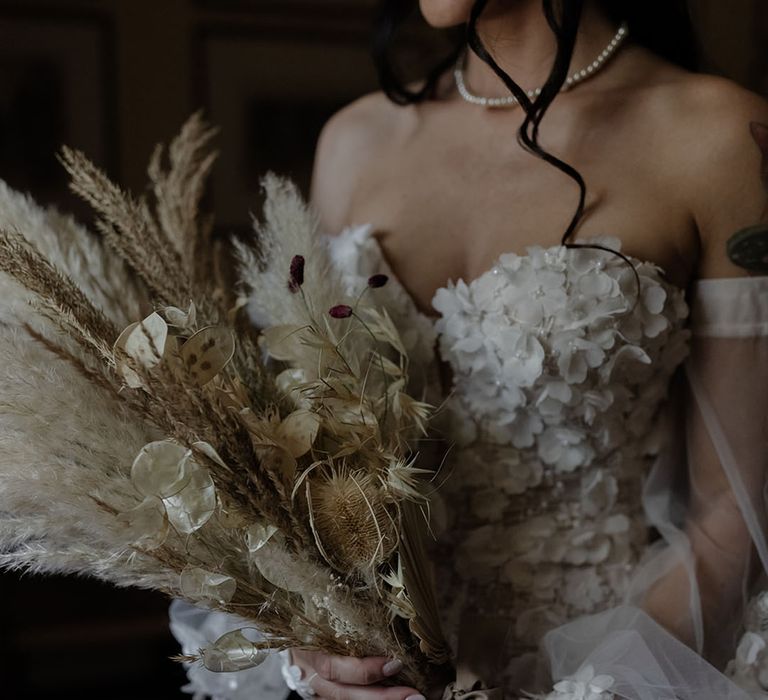 Bride wears appliqué Pronovias wedding dress whilst holding pampas grass bouquet 