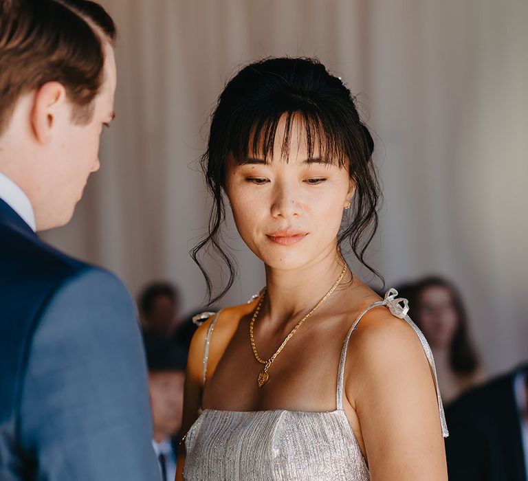 East Asian bride wears silver The Vampire's Wife dress and wears her dark hair in low up do with gold necklace 