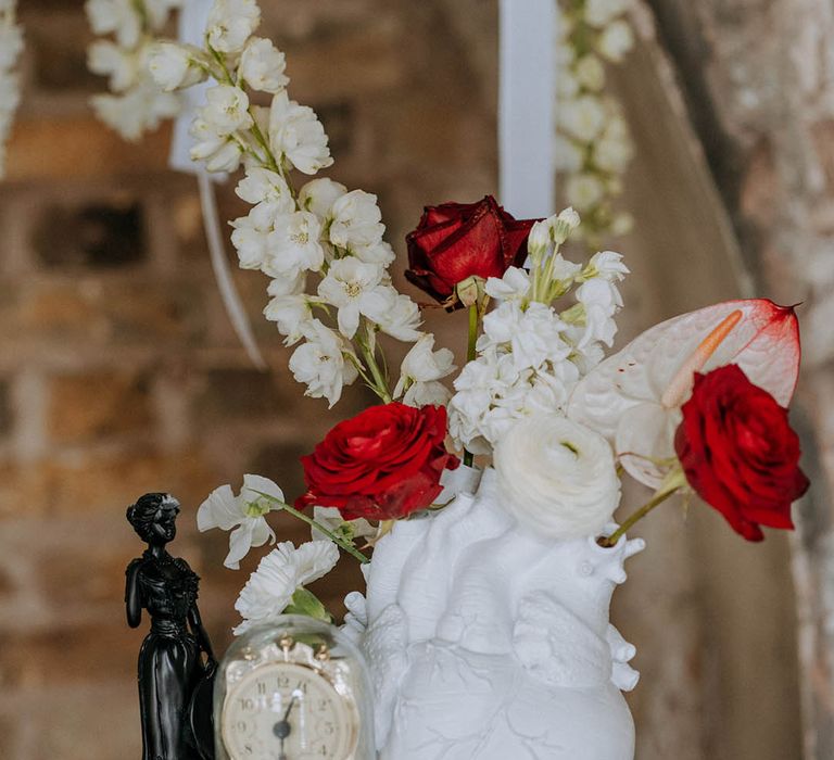 Black red and white wedding decor - white ceramic anatomic heart vase with red roses and chrysanthemums, gold vintage clock in glass dome case and small black woman sculpture