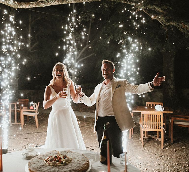 Bride & groom stand beside sparklers as they cut their wedding cake 