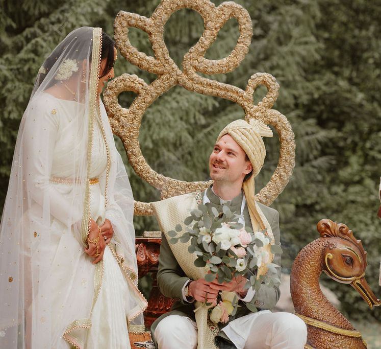 Groom in a green Sherwani holding a bouquet under a mandal with his South Asian bride in a cream lehenga 