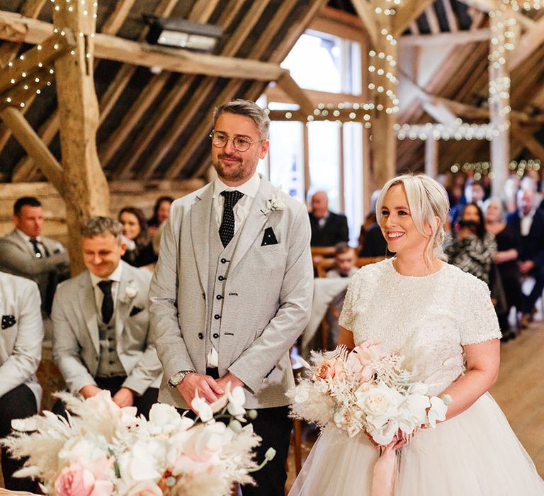 Fairy lit barn wedding venue in Hampshire with the bride and groom standing at the altar for their ceremony 