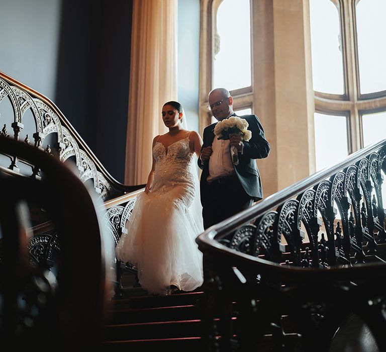 Bride in sleeveless v neck Enzoani wedding dress with tulle finish and church length veil going down the stairs at Grittleton House with father of the bride 