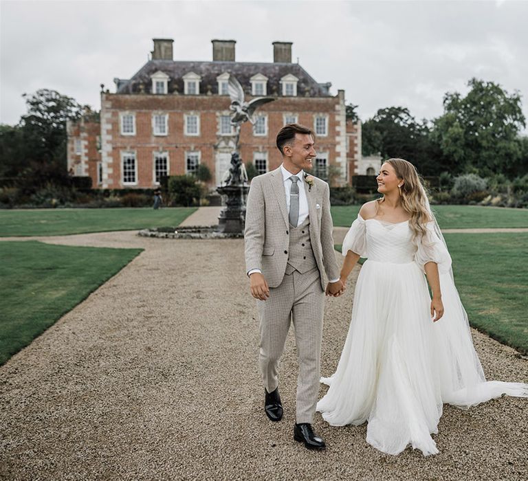 St Giles House country house wedding venue in Dorset with the bride and groom walking along hand in hand 