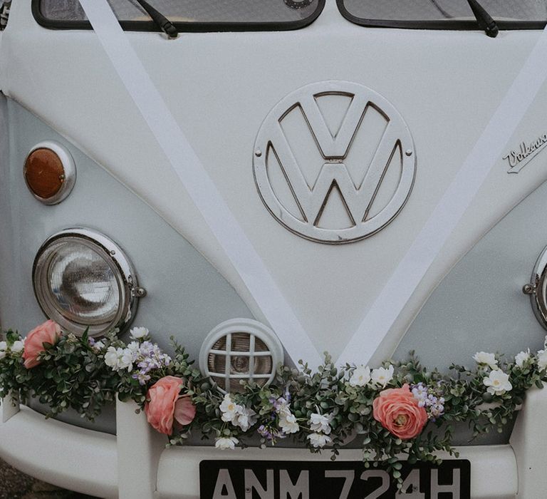 The VW camper van wedding car decorated with white ribbon and pink flowers on the bumper 