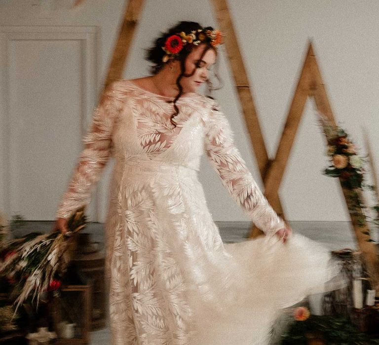 Bride in boho long sleeve 3D applique wedding dress twirling in front of wooden triangular wedding arches 