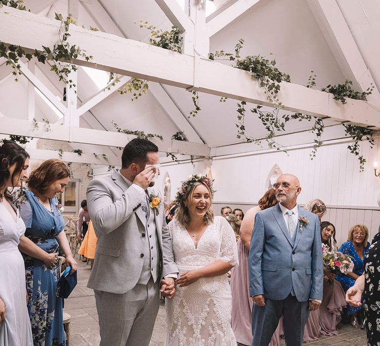 Groom wipes away his tears as he sees the bride in her wedding outfit with the father of the bride in cool sunglasses 