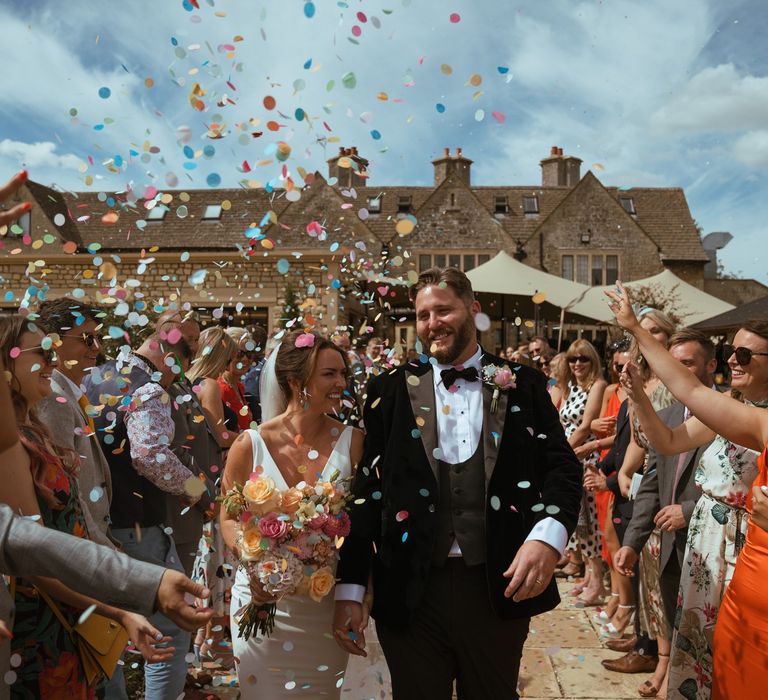 Colourful wedding confetti fluttering down over the bride and groom at their outdoor wedding 