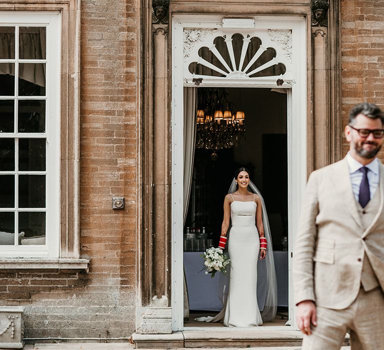 Bride in fitted slip wedding dress with midriff cutout waiting for a first look moment with the groom 