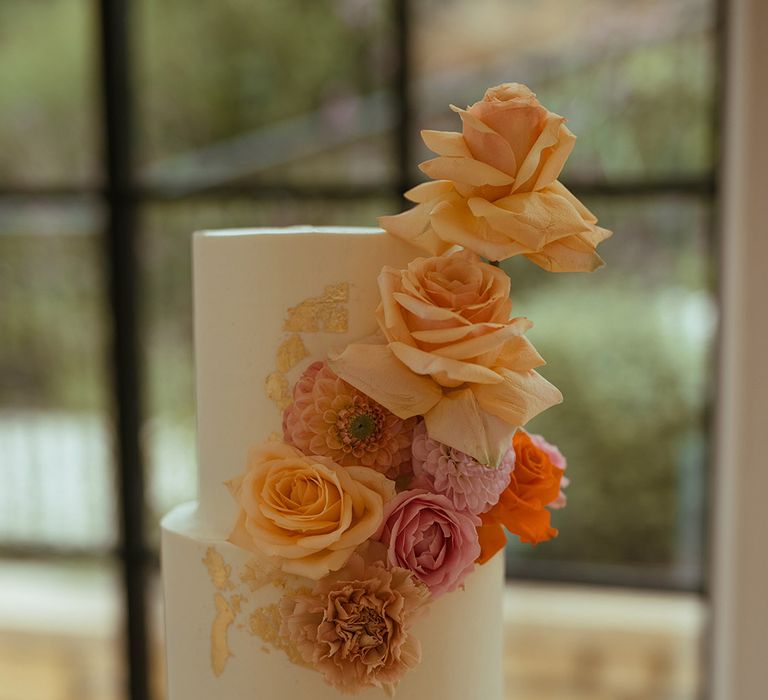 Two tier white frosted wedding cake decorated with pink and orange rose cake decorations