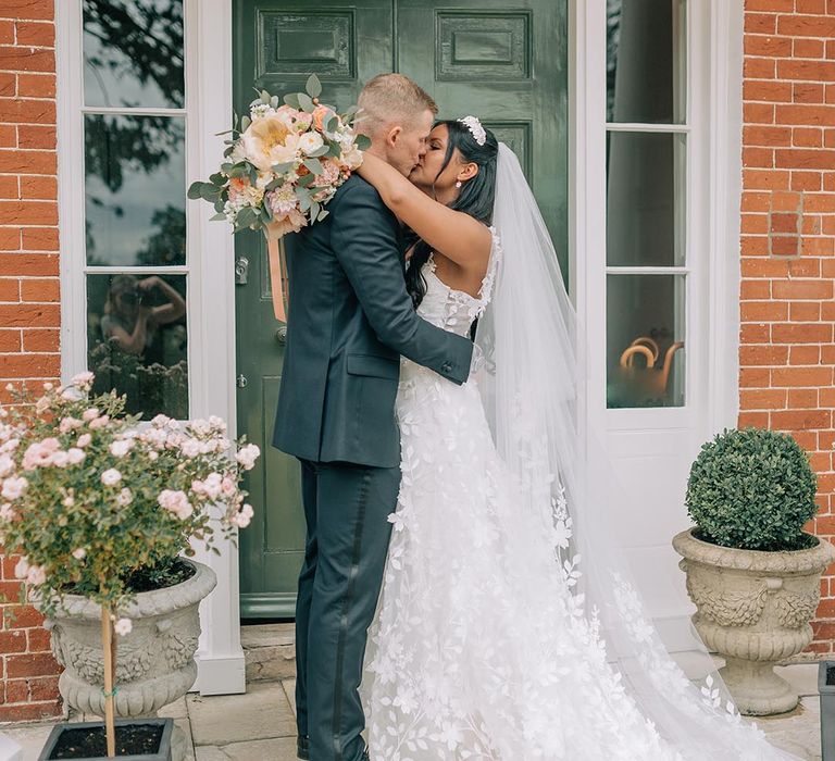 Bride in Savin London wedding dress kissing the groom at the main entrance to their wedding venue 