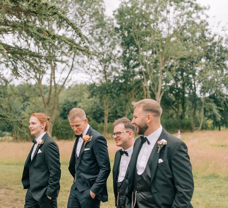 The groom and groomsmen walk together wearing matching black tuxedos 