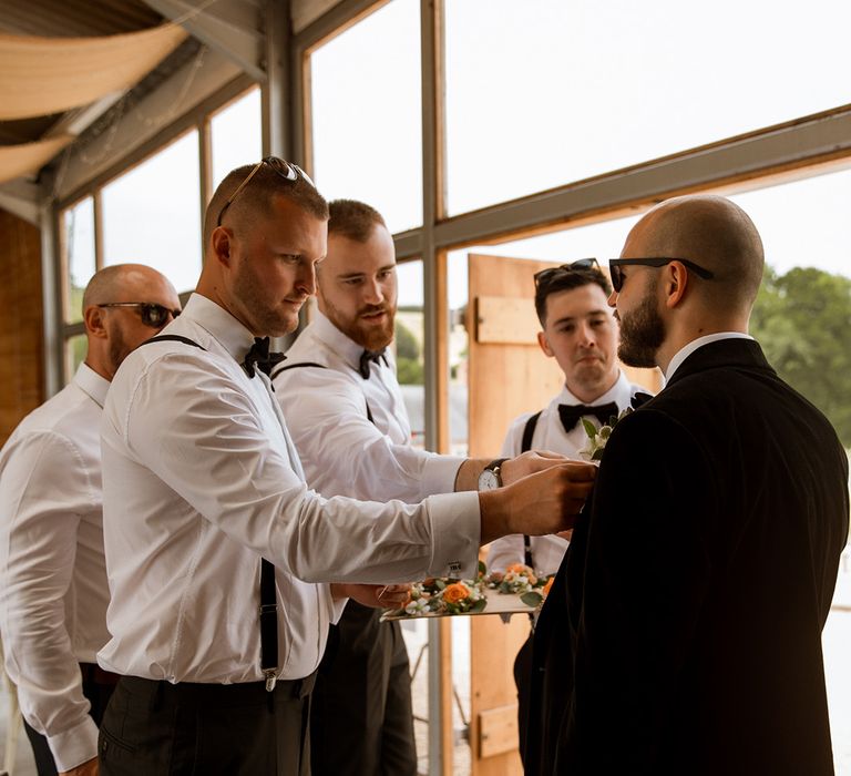 Groomsmen in black tie helping the groom put on their buttonhole 