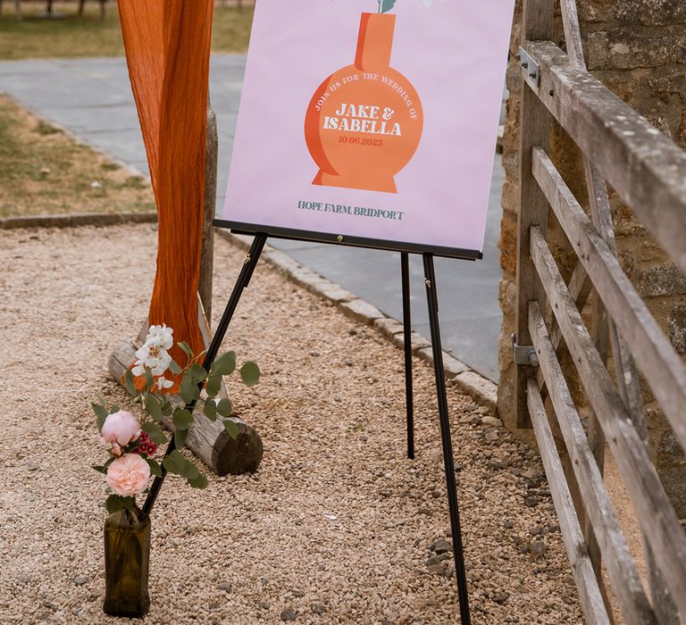 Purple and orange wedding welcome sign with vase of wedding flowers at retro wedding 