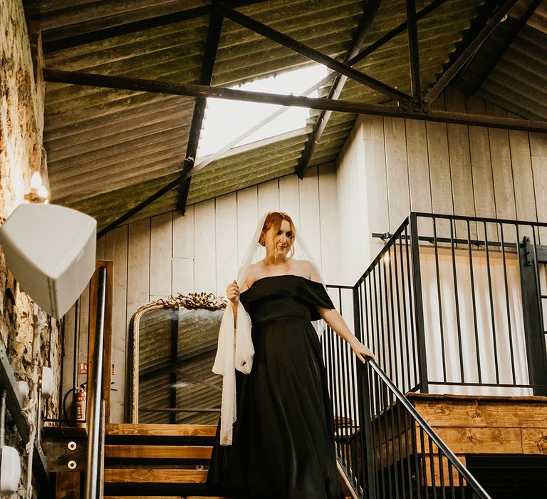 Bride in black satin wedding gown with pearl embellished white veil walking down the stairs 