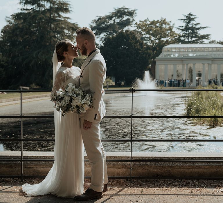 bride and groom portrait in front of Gunnersbury Park wedding venue in a long sleeve wedding dress and beige suit 