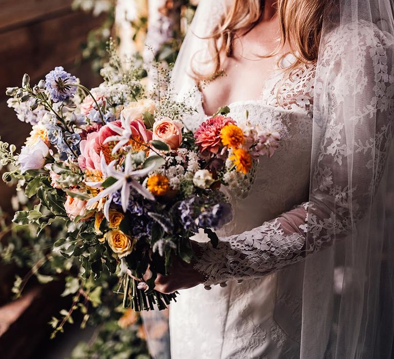 Bride in long sleeve lace wedding dress holding pastel wedding bouquet 