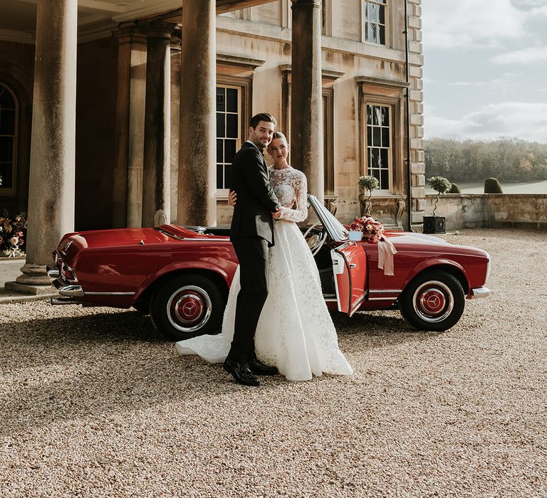 Bride and groom at Prestwold Hall with red wedding car 