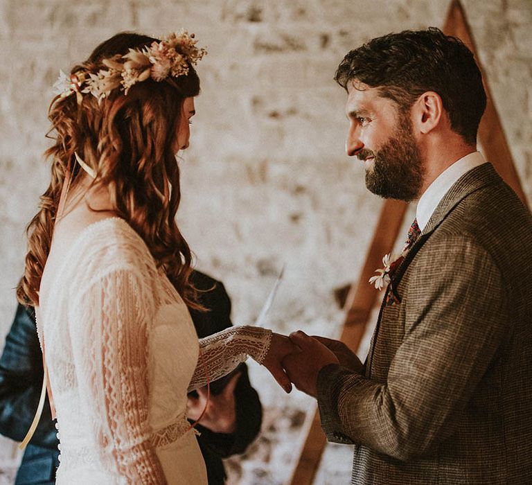 Bride wearing boho flower crown with the groom at the wedding ceremony holding hands as they exchange rings 